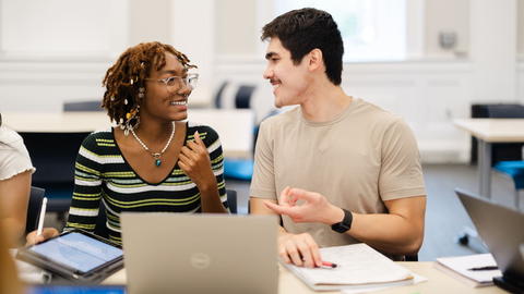 Two students talking in front of a laptop.