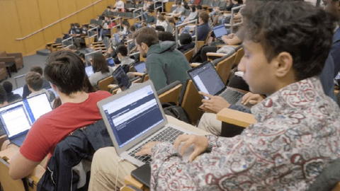 Students sit in rows with their laptops in a lecture hall.
