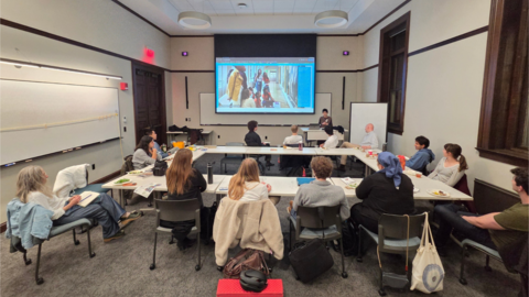 Students around a table looking at a screen with images of students on it