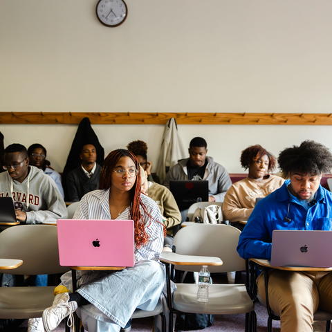 Students seated in a classroom with laptops out and have their attention to the front.