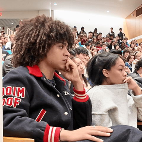A lecture hall full of students watch a debate.
