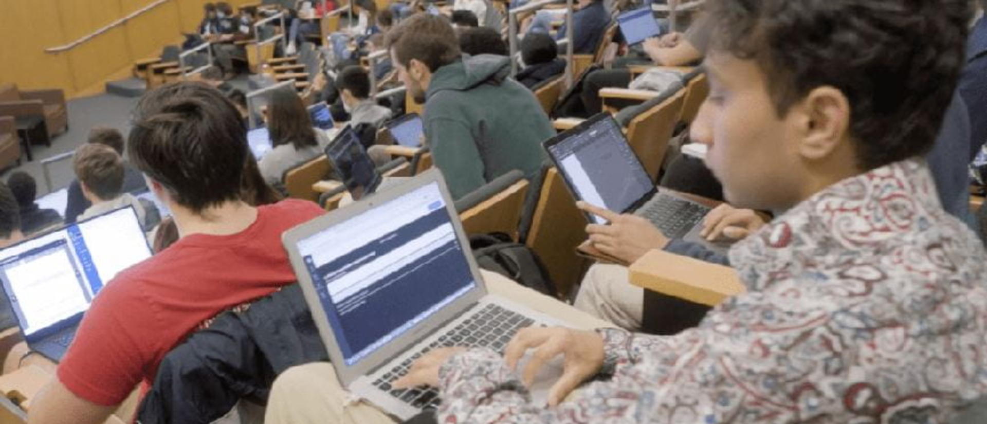 Students sit in rows with their laptops in a lecture hall.