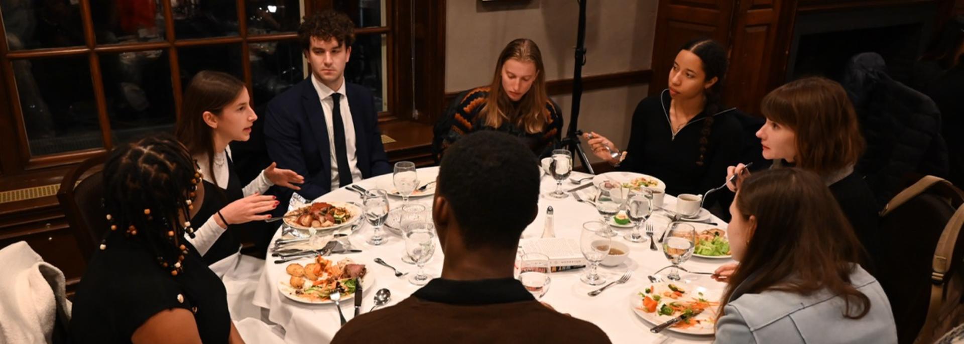 A group of students and faculty converse over dinner.