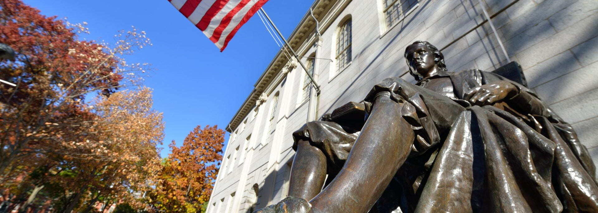 The John Harvard statue on a bright sunny day in Harvard Yard